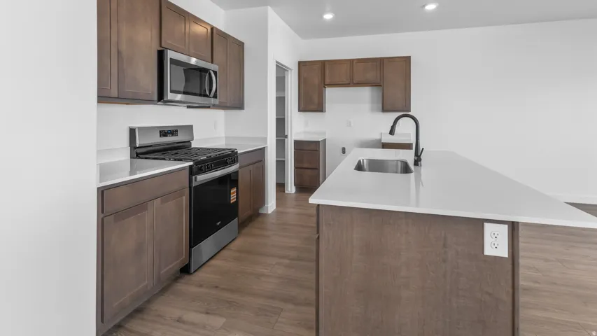 Kitchen featuring wood-finish cabinetry, stainless steel appliances, a center island with a sink, white countertops, and wood-finish flooring