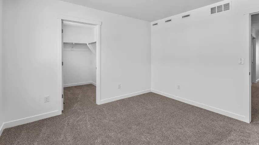 Neutral tone wall paint, textured carpeting, and a walk-in closet with built-in shelving and hanging rod