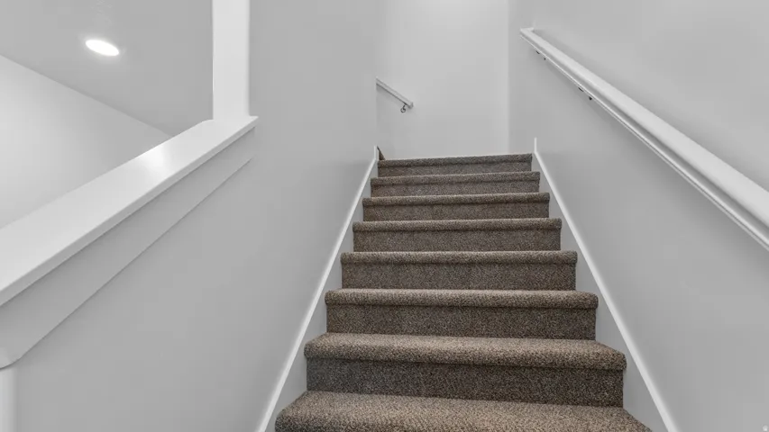 Carpeted staircase with white handrails and recessed lighting