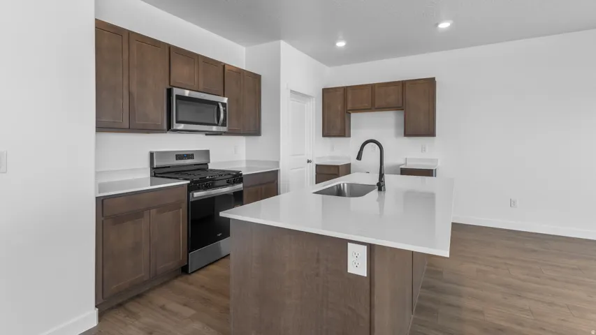 Kitchen featuring wood-finish cabinetry, stainless steel appliances, solid surface countertops, a kitchen island with an undermount sink, and wood-finish flooring