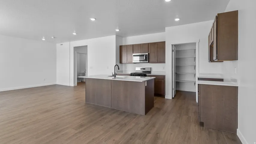 Open-concept kitchen and living area featuring wood-finish flooring, recessed lighting, and a kitchen island with a sink