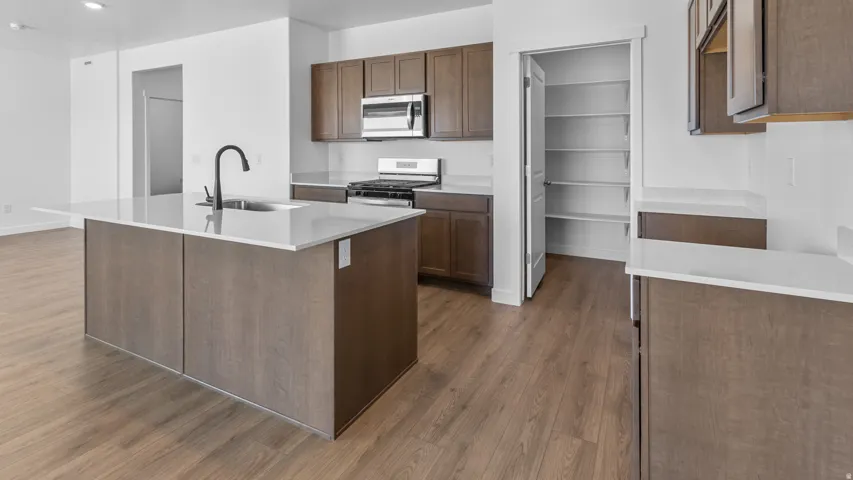 Kitchen featuring a central island with a sink, wood-finish flooring, stainless steel appliances, and a pantry with shelving