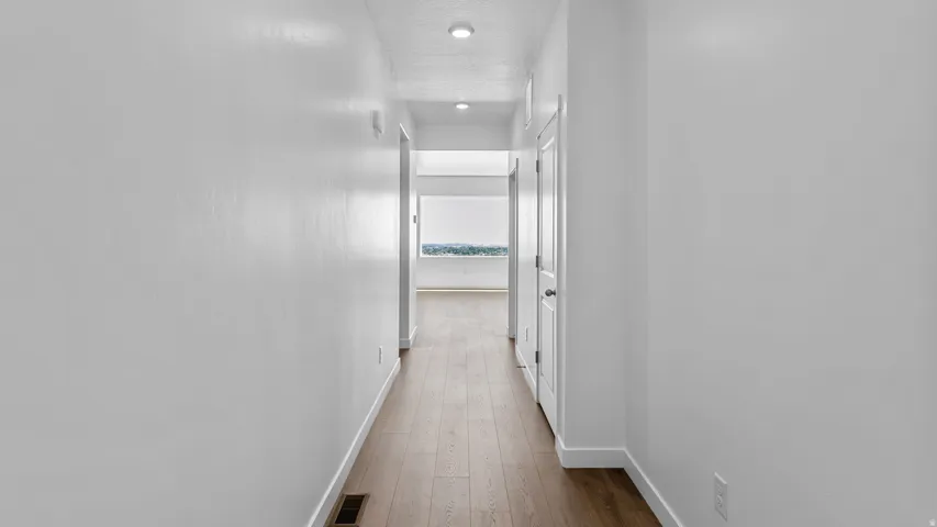 Hallway featuring wood-finish flooring, recessed lighting, and white interior doors