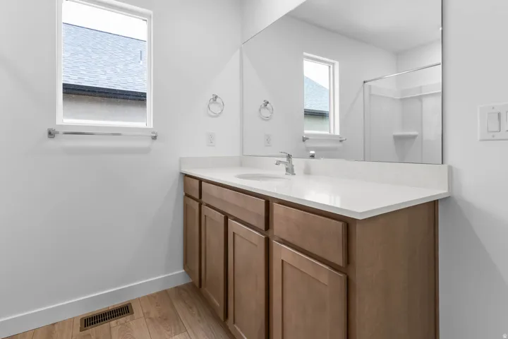 Wood-finish flooring, single vanity with light-toned cabinetry, integrated sink, and a large wall mirror