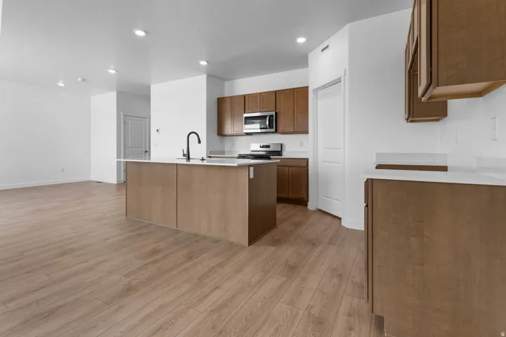 Open-concept kitchen with wood-finish flooring, recessed lighting, and a kitchen island featuring a sink with a black gooseneck faucet