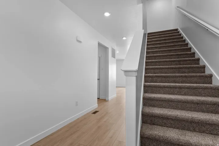 Carpeted staircase with white railing, recessed ceiling lighting, and wood-finish flooring