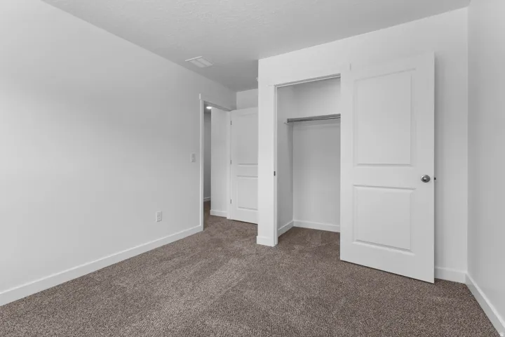 Neutral tone wall finish, textured ceiling, light grey carpet flooring, white trim, and a bi-fold closet with hanging rod