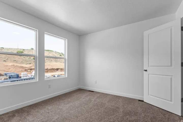 Neutral wall color, two large windows, textured carpeting, and a paneled interior door