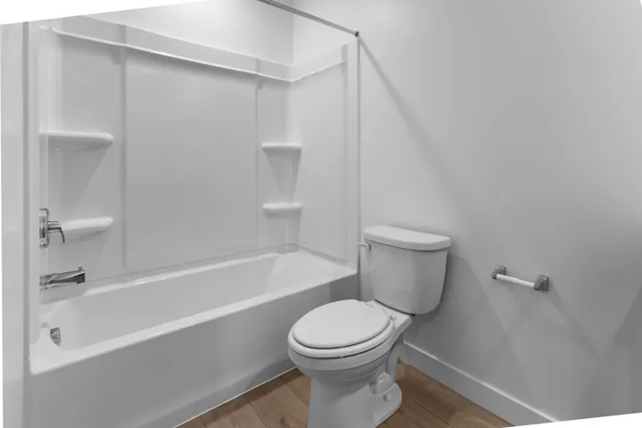Integrated tub and shower combination with white surround, chrome fixtures, and wood-finish flooring
