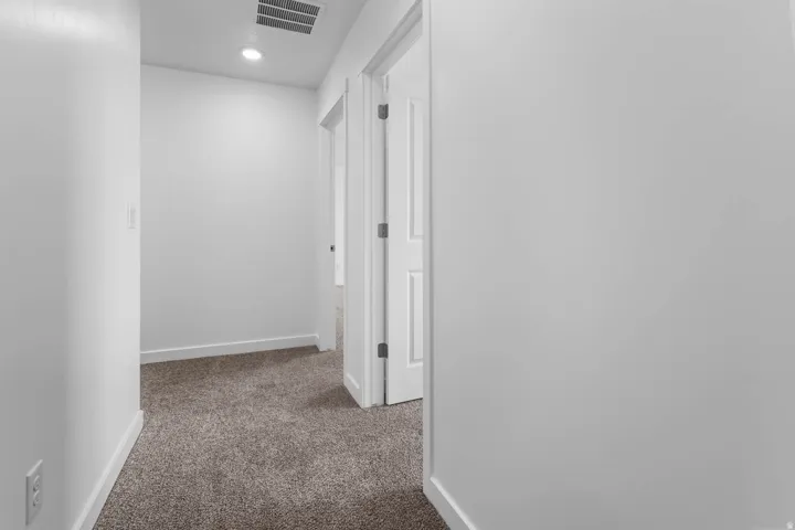Recessed lighting illuminating a hallway with neutral carpeting