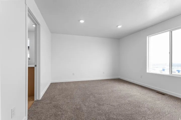 Neutral-toned carpeted flooring, white walls, recessed ceiling lighting, and a large window