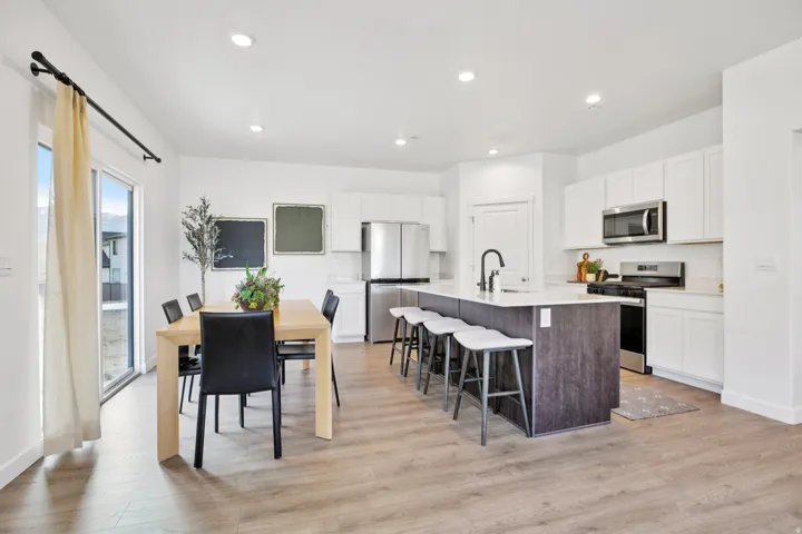Spacious kitchen featuring white cabinetry, stainless steel appliances, a center island with seating, and wood-finish flooring