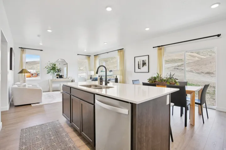 Kitchen island featuring a light-toned countertop, wood-finish cabinetry, and a built-in stainless steel dishwasher