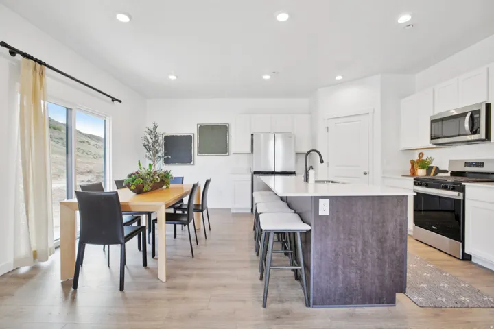 Modern kitchen featuring an island with a light-toned countertop, stainless steel appliances, white cabinetry, and wood-finish flooring