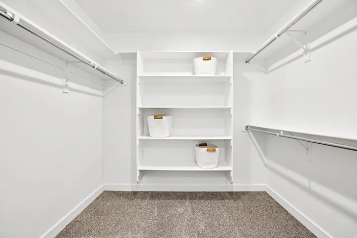 Walk-in closet with built-in shelving, multiple hanging rods, and carpet flooring