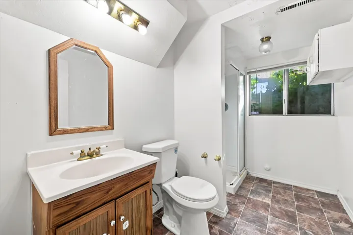 Bathroom featuring a wood-finish vanity with an integrated sink, a glass-enclosed shower, and a window for natural light