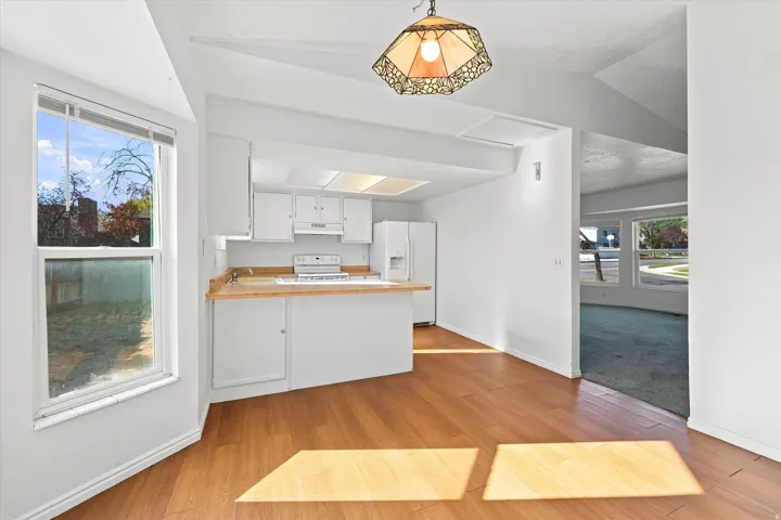 Wood-finish flooring with a bay window, a kitchen featuring white cabinetry, and a built-in range
