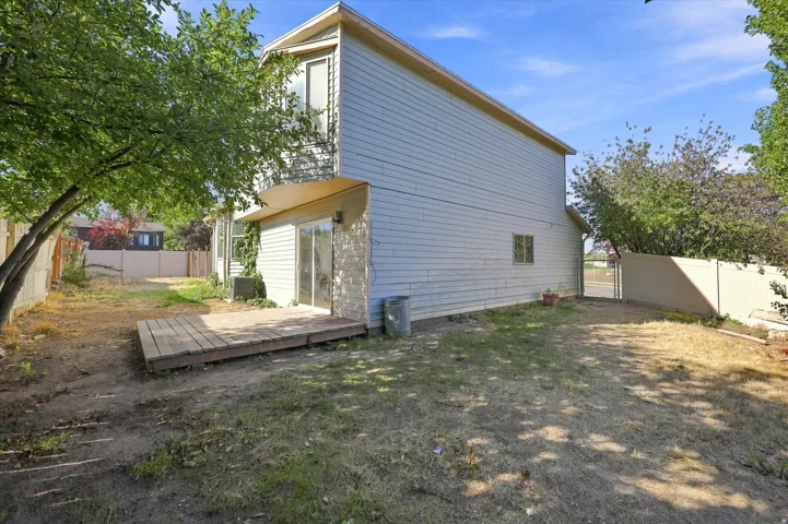 Expansive outdoor space featuring a wood deck, sliding glass door, mature tree, and privacy fencing