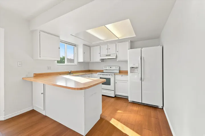 Kitchen featuring white cabinetry, wood-finish flooring, white appliances, a breakfast bar, and a skylight