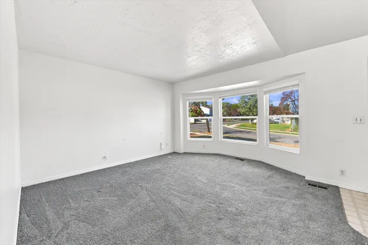 Bay window with multiple panes, vaulted ceiling, neutral wall paint, and grey carpet flooring