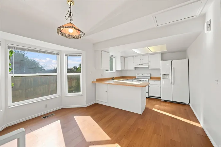 Kitchen and dining area featuring wood-finish flooring, white cabinetry, integrated appliances, and a bay window