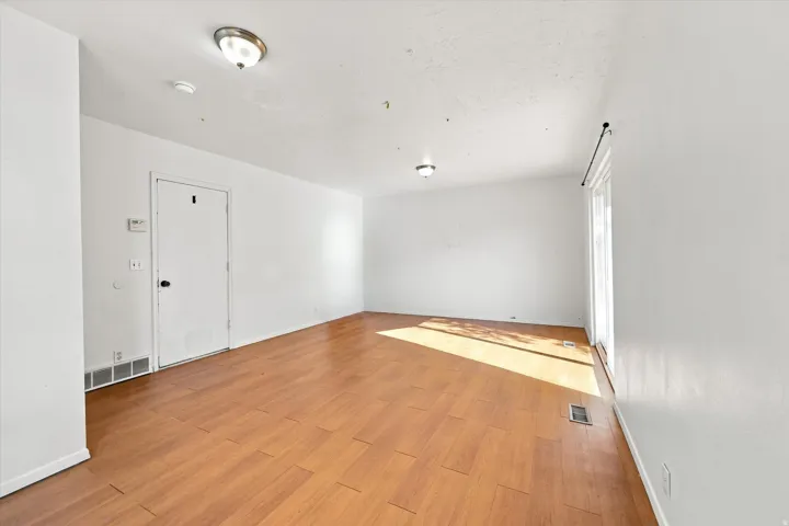 Spacious room featuring wood-finish flooring, white walls, and a sliding glass door
