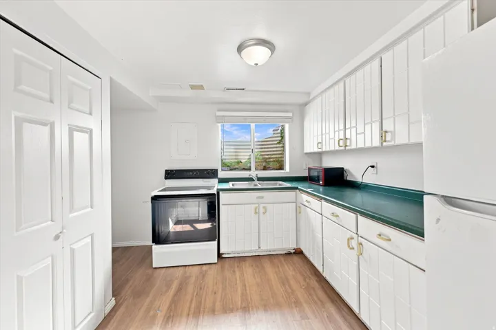 Kitchen featuring white cabinetry, a single basin sink, a white range, a white refrigerator, and wood-finish flooring