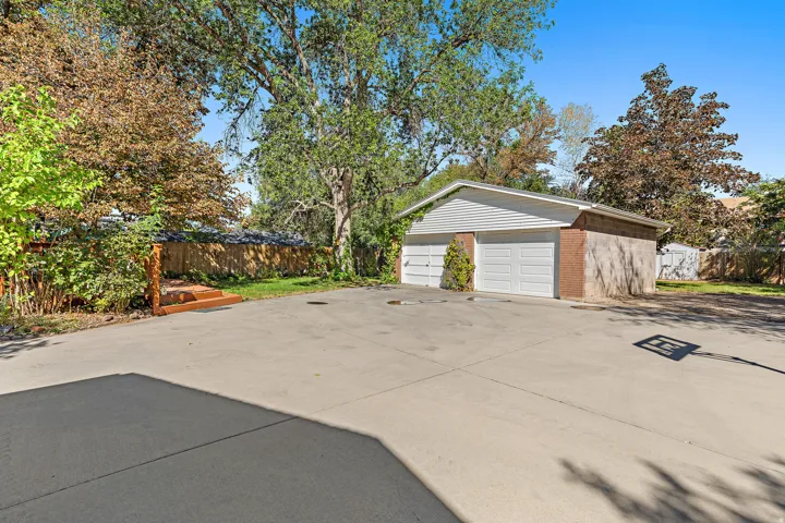 Detached two-car garage with overhead doors, concrete driveway, wood privacy fence, and mature trees