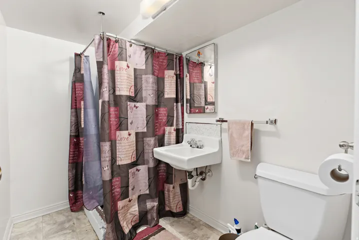 Basement bathroom, wall-mounted sink, toilet, and shower with a curved curtain rod. Shower is not fully finished.