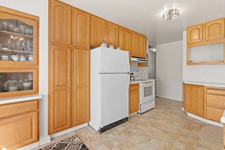 Wood-finish cabinetry with glass-front display, white countertops, and tiled flooring
