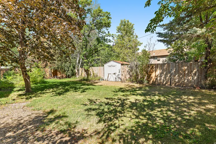 Expansive green lawn, mature trees providing shade, privacy fencing, and a permanent storage shed