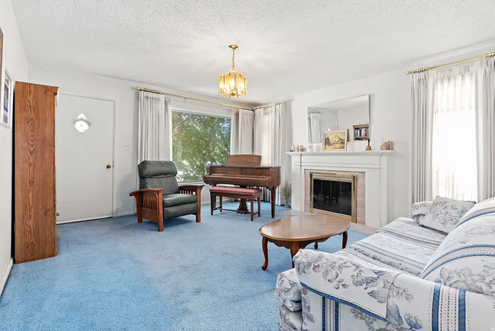 Living area featuring a fireplace with a white mantel, large windows with curtain rods, and a ceiling-mounted light fixture