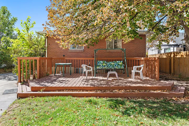 Expansive outdoor deck with wood-finish railing and steps, set against a brick exterior, and surrounded by mature trees