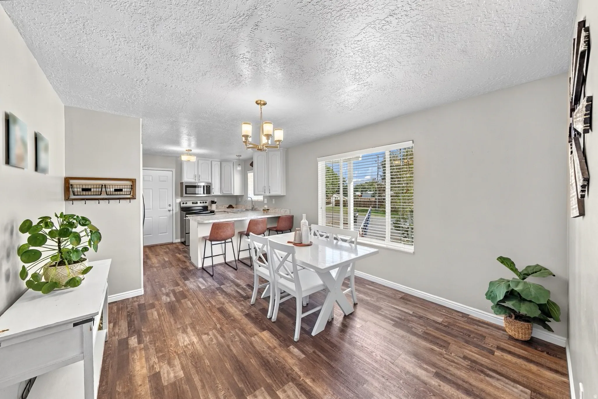 Open-concept dining area with wood-finish flooring, a window with blinds, and an overhead chandelier