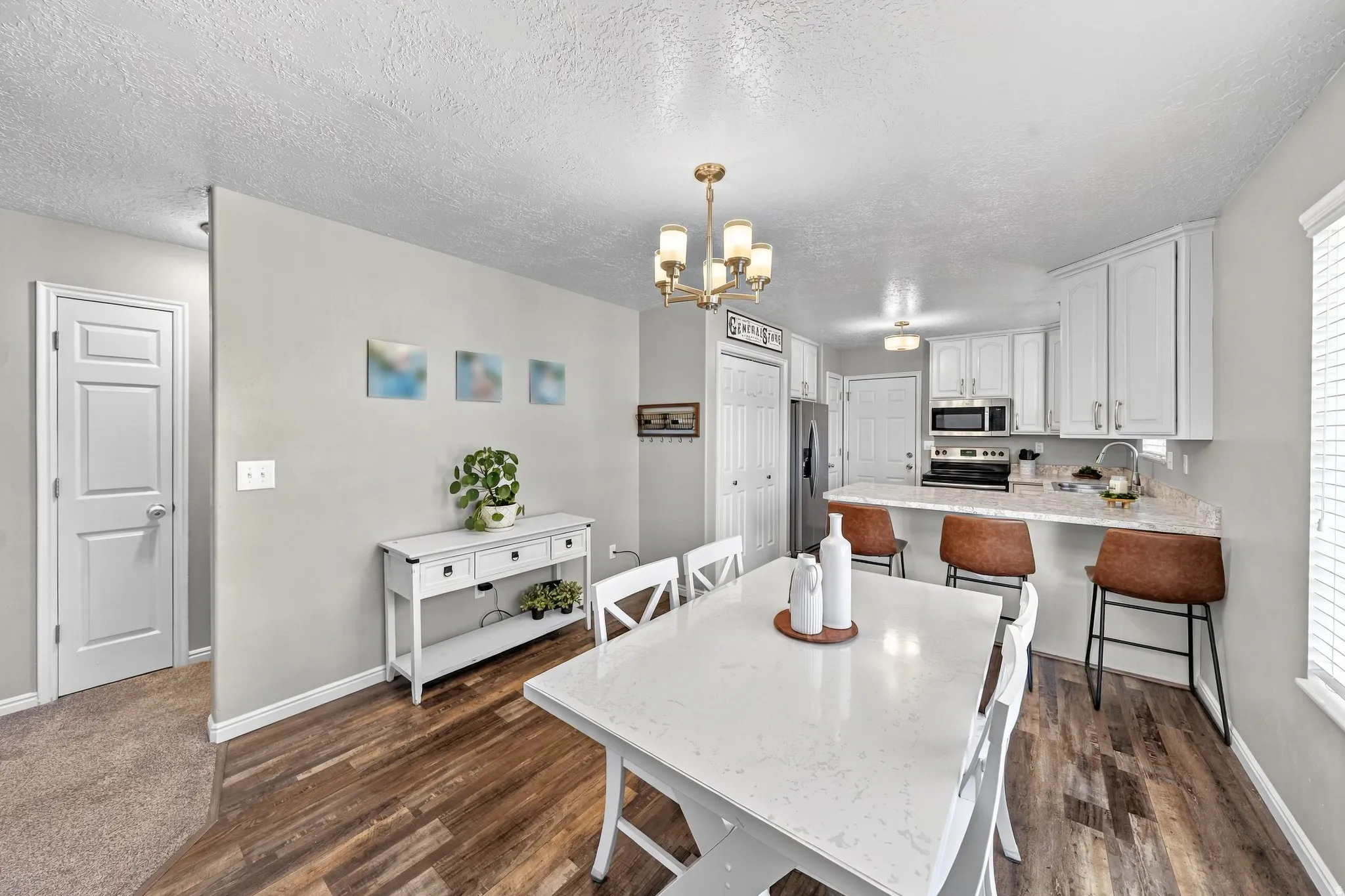 Open-concept dining area featuring wood-finish flooring, a contemporary chandelier, and a breakfast bar with white cabinetry and integrated appliances