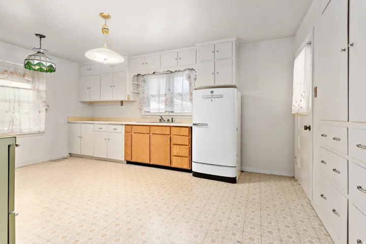 Kitchen featuring white upper cabinetry, light wood-finish lower cabinetry, a stainless steel sink, and patterned flooring