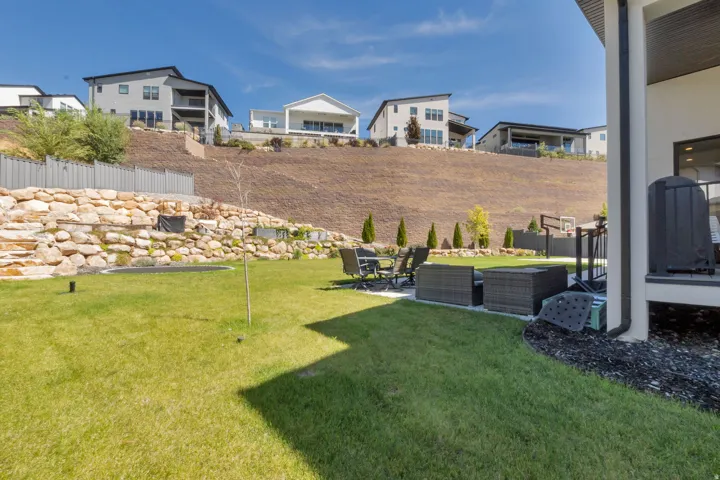 Expansive backyard featuring a lush lawn, stone retaining wall, and a paved patio area