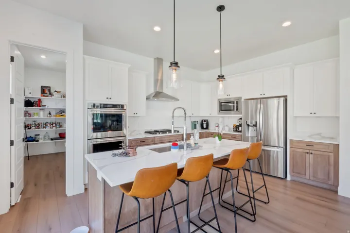Gourmet kitchen with stainless stee Kitchenaidl appliances, white cabinetry, a spacious central island with a sink, pendant lighting, and wood-finish flooring