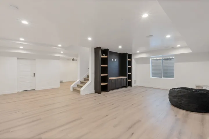 Spacious room featuring light wood-finish flooring, recessed lighting, a custom built-in media center with shelving, and a paneled white door