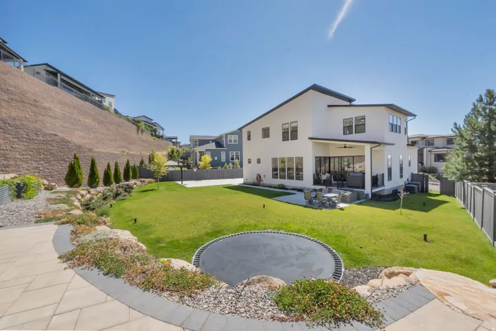 Expansive backyard featuring a manicured lawn, built-in trampoline, and a paved patio area