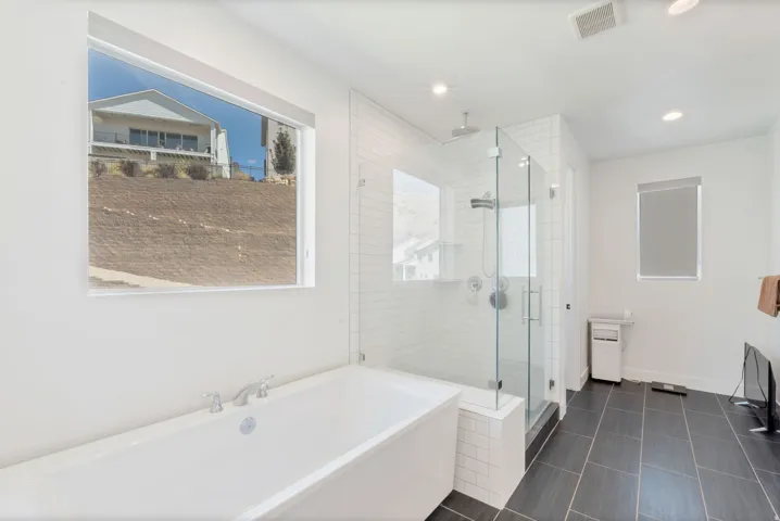 Soaking tub with chrome fixtures, glass-enclosed shower with subway tile surround, dark tile flooring, and recessed lighting
