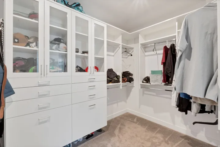 Custom closet system featuring built-in cabinetry, glass-front doors, multiple drawers, shelving, and hanging rods