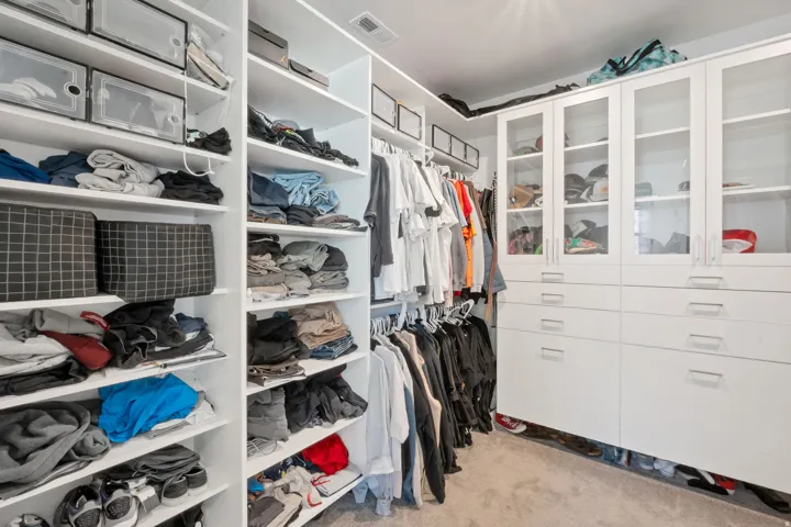 Built-in closet system featuring white shelving, multiple hanging rods, and integrated cabinetry with glass-front uppers and drawer storage