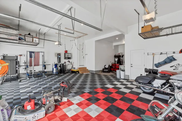 Spacious garage with checkered tile flooring, high ceilings, built-in overhead storage racks, and multiple access doors