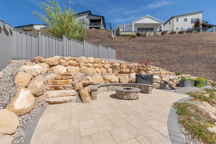 Paver patio featuring a built-in smokeless fire pit, stone retaining walls, and integrated stone seating
