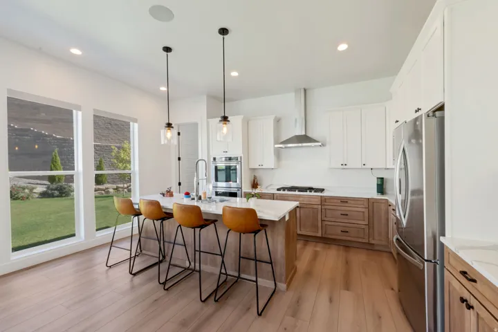 Expansive kitchen with wood-finish flooring, a large island with a light-toned quartz countertop, and pendant lighting