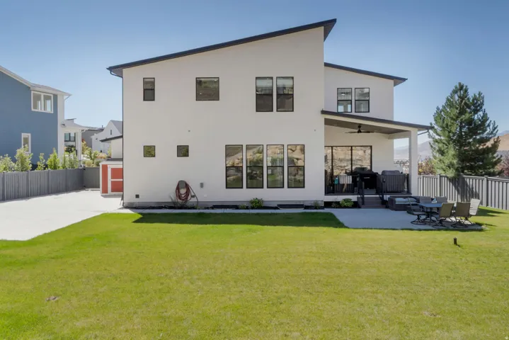 Modern exterior with a sloped roofline, expansive lawn, concrete patio, covered outdoor living area with ceiling fan, and large windows