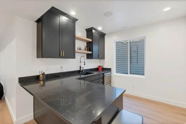U-shaped dark countertop with integrated sink, black cabinetry, wood-finish flooring, recessed lighting, and a built-in dishwasher