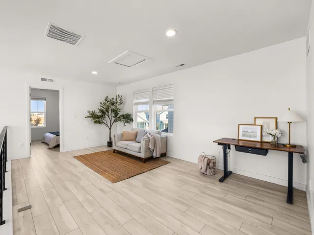 Light wood-finish flooring throughout, multiple windows with blinds, recessed lighting, and white walls