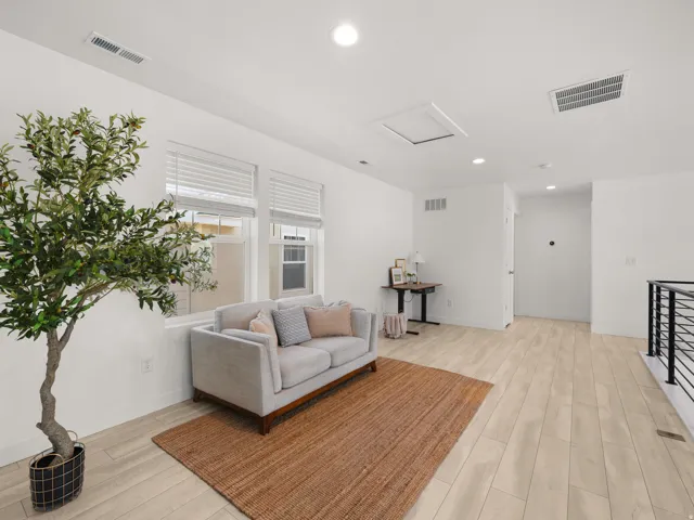 Recessed lighting illuminates the open area, featuring light wood-finish flooring and multiple windows